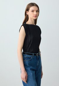 Top nero plissettato con maniche a cappuccio e scollatura rotonda, abbinato a jeans in denim blu a vita alta e una cintura nera.