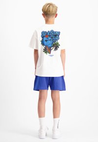 Witte t-shirt met een kleurrijke graphic van een blauwe ijscrème figuur met een kers bovenop, omringd door palmbomen. Gedragen met blauwe shorts.