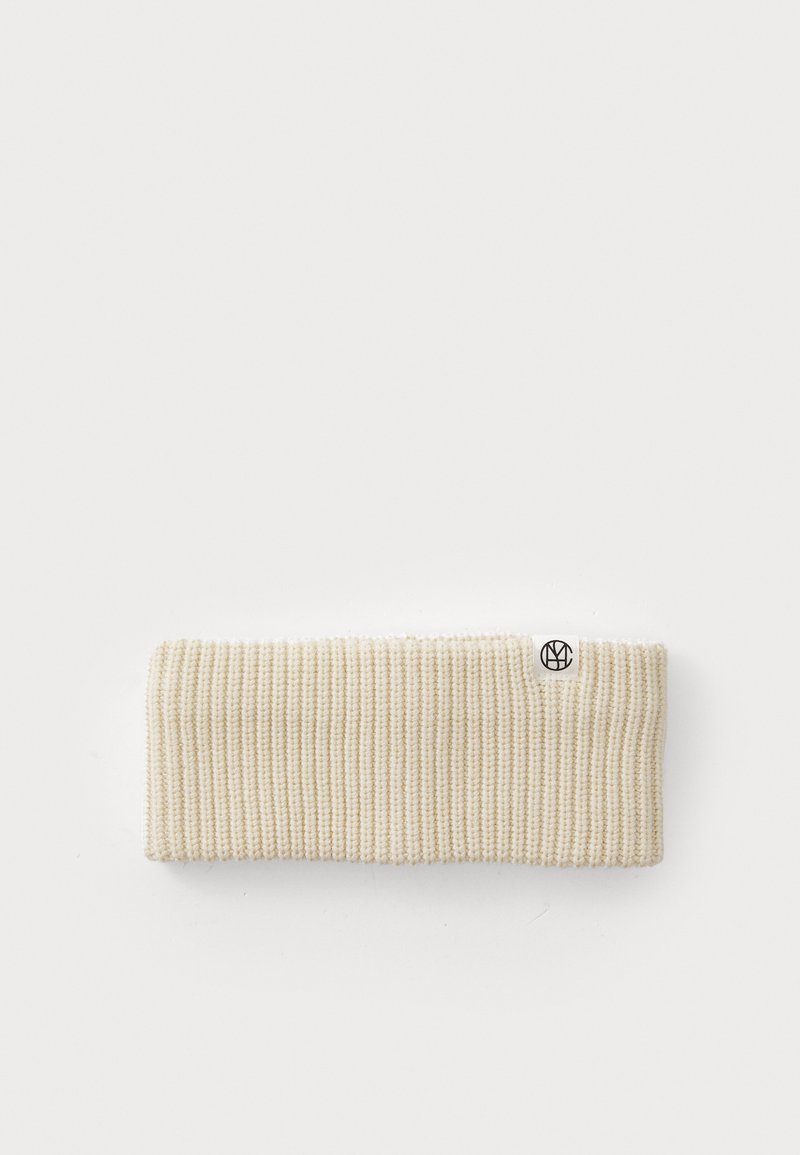 Knit headband in light beige, featuring a ribbed texture and a small black logo tag on one side. Simple, no additional embellishments.