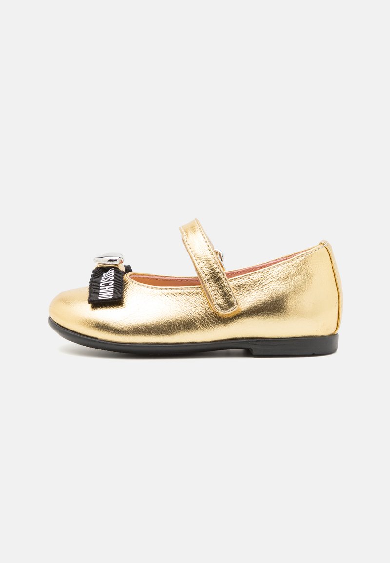 Goldene metallische Mary-Jane-Schuhe mit einem schwarzen Riemen und glänzenden Hardware-Elementen, runder Zehenform und glatter Textur. Schwarze Gummisohle für besseren Grip.