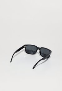 Gafas de sol negras con forma rectangular, montura de plástico, lentes oscuros y varillas delgadas y rectas. Presentan un marcado mínimo en el lateral.