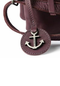 Borsa a mano in pelle color marrone scuro con superficie testurizzata, sottili cinturini e una targhetta metallica rotonda con emblema ad ancora e dettaglio di cuciture.