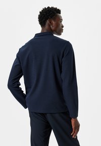 Tummansininen, pitkähihaisessa poolopaidassa on teksturoitu kangas ja litteä kaulus. Siinä on rento leikkaus ja huomaamattomat ommeltu yksityiskohdat helmassa.