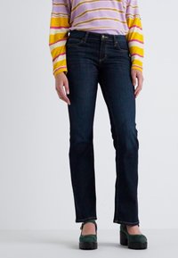 Dark blue jeans with a straight leg cut, worn with a striped long-sleeve shirt. Shoes are green platform with a chunky sole.