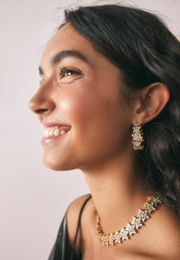 Cercei în formă de stea aurie și un colier asortat au accente din cristale clare. Textura netedă a metalului completează o bluză neagră.