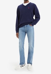 Suéter de punto azul marino con cuello en V, jeans rectos de pierna recta azul claro y zapatillas blancas con detalles en negro. El suéter tiene un pequeño detalle de logotipo rojo.