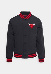Svart varsityjacka med röd och vit randig ribbad krage och manschetter. Har en broderad tjurlogotyp på vänster bröst.