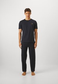 Męski zestaw ciemnoniebieskiego bawełnianego odzieży do relaksu składający się z koszulki typu crew neck i pasujących spodni. Spodnie mają luźny krój i elastyczny pas.