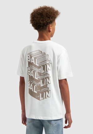 Tiener met krullend haar, gekleed in een wit T-shirt met gestapelde boeken en het woord "BALLIN" gedrukt op de achterkant.