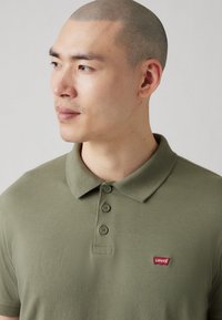 Polo verde măsliniu din bumbac, cu guler clasic, trei butoane și un mic logo Levi's roșu pe pieptul stâng.