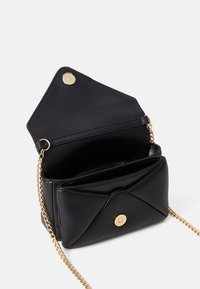 Černá kožená crossbody taška se zlatými kovovými detaily, s zapínáním na knoflík, řetízkem a několika vnitřními přihrádkami.