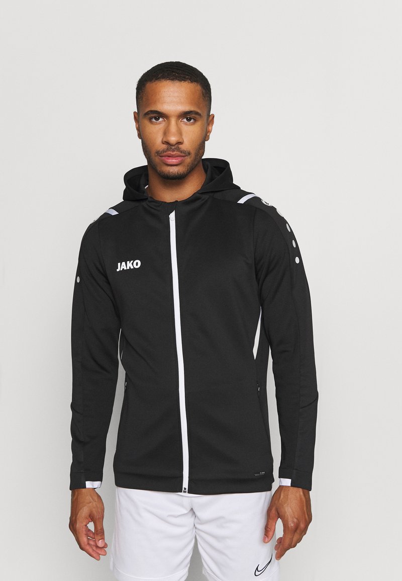 Zwart sportjack met een capuchon, voorzien van witte ritsen, zijkanten en logo. Lange mouwen met knoopdetails op de schouders.