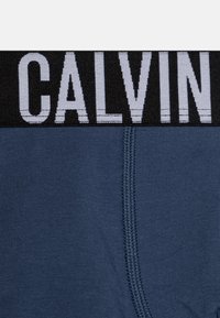 Marineblauwe katoenen boxershorts met een zwarte elastische tailleband waarop "CALVIN" in vetgedrukte witte letters staat en een gladde textuur heeft.