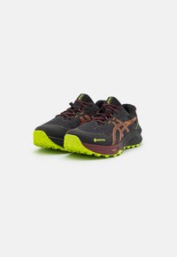 Sorte turstøvler med lys grønn yttersåle, oransje detaljer, teksturerte stoffoverflater og polstrede såler, med en GORE-TEX etikett.