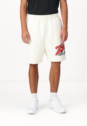 Shorts bianchi in cotone con vita elastica, caratterizzati da una grafica rossa sulla gamba sinistra. Abbinati a sneakers bianche e calze alte.