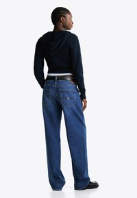 Navy gebreide cropped hoodie met een textuurpatroon, gecombineerd met hoge taille, losvallende blauwe denim jeans. Zwarte platte schoenen maken de look compleet.
