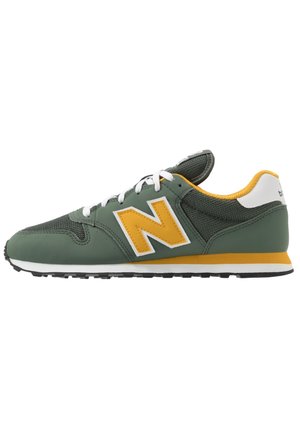 Groene en mosterdgele sneaker met witte veters, mesh en lederen bovenwerk, en een groot mosterdkleurig "N"-logo aan de zijkant, gezien vanaf de buitenkant.