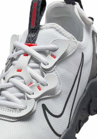 Witte sport schoen met een bovenwerk van mesh, grijze accenten, rode veters en een kenmerkend zwart swoosh-logo. Heeft een gestructureerde zool voor grip.