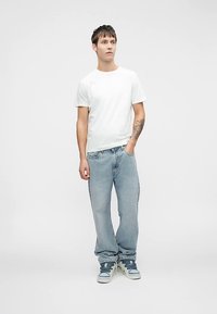 Balti medvilninė marškinėlių pora su šviesiai mėlynais laisvo stiliaus džinsais ir pilkais sportbačiais. Paprastas dizainas, be matomų raštų ar akcentų.