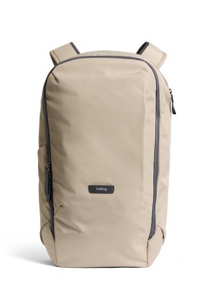 Zaino beige in tessuto resistente, caratterizzato da un design lineare, cerniere nere e spallacci regolabili. Logo del marchio ben visibile sul davanti.