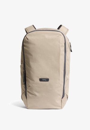 Zaino beige in tessuto resistente, caratterizzato da un design lineare, cerniere nere e spallacci regolabili. Logo del marchio ben visibile sul davanti.