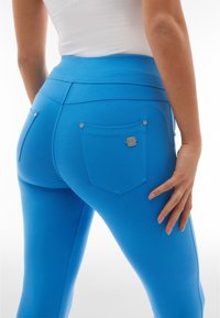 Leggings blu realizzati in tessuto elasticizzato, con una vita alta, due tasche posteriori e accenti metallici vicino ai bordi delle tasche.