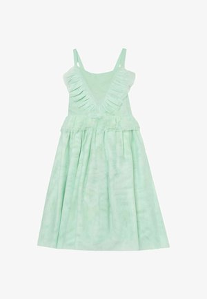 Junges Mädchen mit langen blonden Haaren, das ein hellgrünes ärmelloses Kleid trägt und die Seiten des Rocks hält, vor einem einfarbigen Hintergrund.
