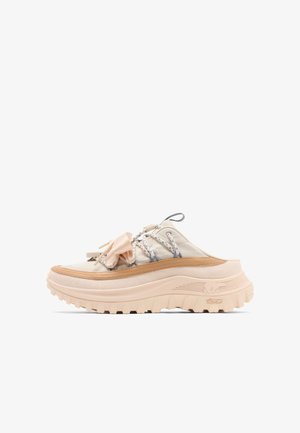 Beige slip-on-sneaker med tyk rillede såler, dekorative snørebånd og stofsløjfe på oversiden.