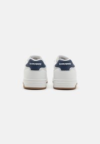 Zapatillas blancas con un upper de cuero suave, un acento en azul marino en el talón y una suela de goma color caramelo. Presenta una marca mínima en la parte posterior.