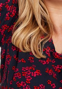 Camisa de marina con patrón floral rojo, textura suave, cuello redondo y mangas cortas. Presenta pequeñas flores en diferentes tonalidades de rojo.