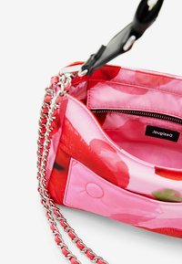 Borsa con motivo floreale rosso e rosa, dotata di una tracolla in catena silver, texture liscia e una tasca interna con zip, caratterizzata da un'etichetta del logo.
