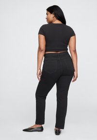 Črna kratka majica združena s črnimi ozkimi kavbojkami. Kavbojke imajo klasičen dizajn s petimi žepi in subtilne detajle šivanja.