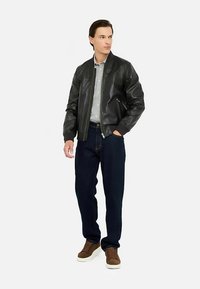 Sort læder bomberjakke med strikkede manchetter og taljebånd, båret over en lysegrå skjorte. Kombineret med mørkeblå jeans og brune sneakers.