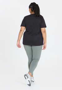 Sort kortærmet t-shirt kombineret med tætsiddende lys grønne leggings og grå sportsko, præget af en glat og elegant tekstur.