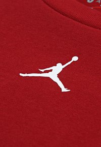 Κόκκινο ύφασμα με ομαλή υφή που απεικονίζει μία λευκή σιλουέτα άλτη που κρατά μια μπάλα μπάσκετ, εμφανώς τοποθετημένη στο ύφασμα.