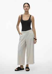 Body nero senza maniche, pantaloni beige chiaro a gamba larga con una texture liscia e cintura elastica, abbinati a sandali neri senza tacco.