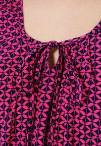 Top de tejido navy con un patrón geométrico rosa, que presenta un escote redondeado y un detalle de lazo en el centro, con pliegues a cada lado.