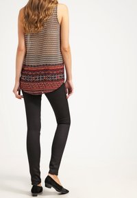 Haut sans manches à motifs géométriques en noir, blanc et rouge, associé à des leggings noirs élégants et des chaussures plates.