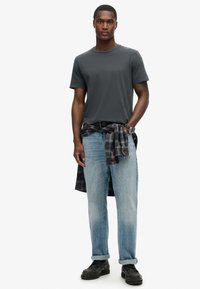 Grå kortærmet t-shirt, lyseblå lige bukser, sorte lædersko og en ternet flannel skjorte bundet om livet.