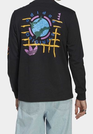 Bagpå sort langærmet skjorte med farverigt abstrakt globusdesign, teksten "adidas Originals" og lilla trefoil-logo, båret med lyseblå jeans.