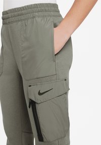 Ljust olivgröna joggers med elastisk midja, sidofickor och en blixtlåsficka på benet som har en svart Nike-logga.
