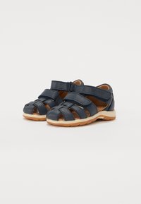 Marineblå lærsandaler med flere stropper, velcro-lukninger og en lys brun gummisål. Åben tå-design med en struktureret overflade.