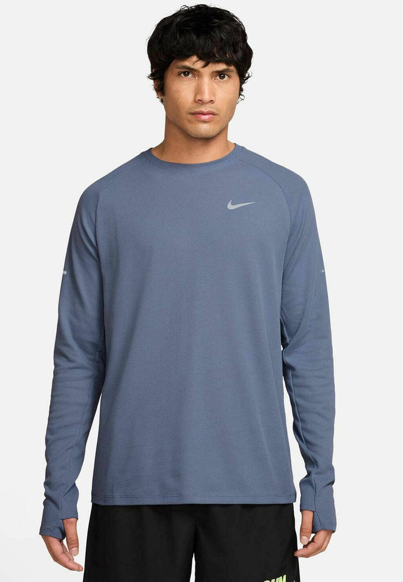 Langarm-Athletikshirt aus strukturiertem, mitteldickem blauen Stoff, mit einem kleinen silbernen Nike-Logo auf der Brust und enganliegenden Bündchen mit Daumenlöchern.