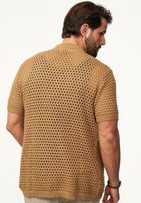 Kurzarmpullover aus leichtem Braun mit Lochmuster, geripptem Kragen und umgeschlagenen Ärmeln, der ein strukturiertes, atmungsaktives Design präsentiert.