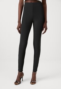 Leggings noirs taille haute avec une texture côtelée et une coupe slim. Assortis à des sandales à talons hauts avec des lanières. Design simple et minimaliste.