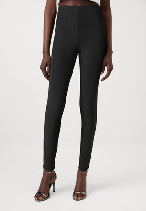 Black, high-waisted leggings with a ribbed texture and slim fit. Paired with strappy, high-heeled sandals. Simple, minimalist design.