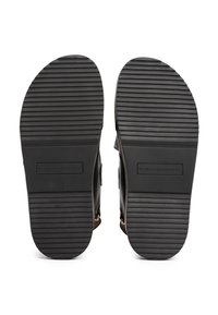 Čierne gumené podrážky sandálov s horizontálnymi drážkami, s vyrazeným logom a hladkým povrchom. Žiadne ďalšie detaily ani ozdoby.