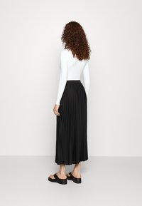 Rosa maxi gonna plissettata nera, a vita alta e con un design fluido. Abbinata a un top bianco aderente a maniche lunghe e sandali neri con plateau.