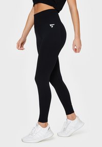 Čierne vysoké legíny z elastickej látky, vystupujúce s hladkým povrchom a malým bielym logom na ľavom boku.