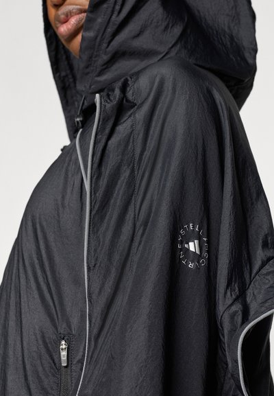 Μαύρο ελαφρύ μπουφάν με κουκούλα από υφή ύφασμα, διαθέτει τσέπη με φερμουάρ και λογότυπο στο μανίκι. Γκρι λεπτομέρειες στα άκρα.